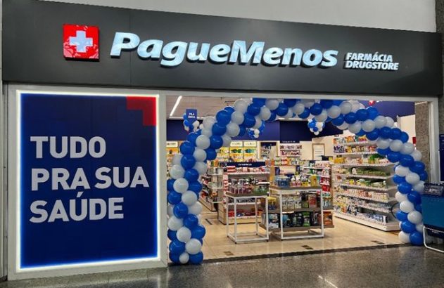 Entrada da Pague Menos Farmácia Drugstore com balões azul/brancos e cartaz 'Tudo pra sua saúde'.