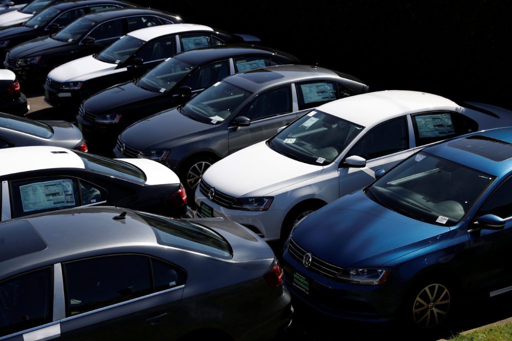 Vista aérea de pátio de concessionária com carros Volkswagen sedans novos, de cores variadas, estacionados.