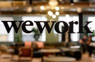 A palavra 'wework' em preto sobre um vidro. Fundo desfocado de um escritório.