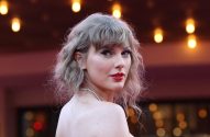 Taylor Swift olhando para trás, cabelo loiro ondulado curto e batom vermelho.