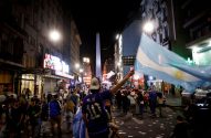 Rua noturna em Buenos Aires com o Obelisco. Multidão celebra, um torcedor com camisa do Messi ergue bandeira argentina.