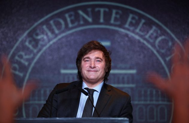 Homem de terno sorrindo com 'Presidente Eleito' ao fundo e mãos em celebração.