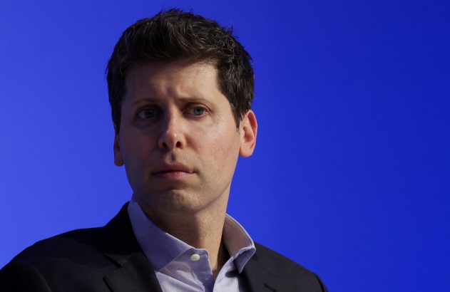 Sam Altman é CEO da OpenAI, dona do ChatGPT, é um homem branco, de olhos azuis, de terno escuro e camisa azul, olhando com expressão séria contra fundo azul.