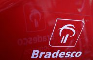 Logotipo branco Bradesco em destaque em superfície vermelha. O símbolo P estilizado e o nome são visíveis, com um leve reflexo.