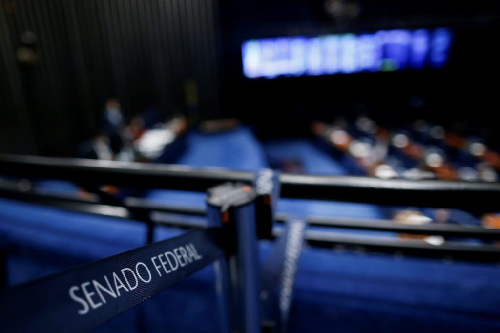 Câmara do Senado Federal com assentos azuis vazios e placa "Senado Federal" em primeiro plano.