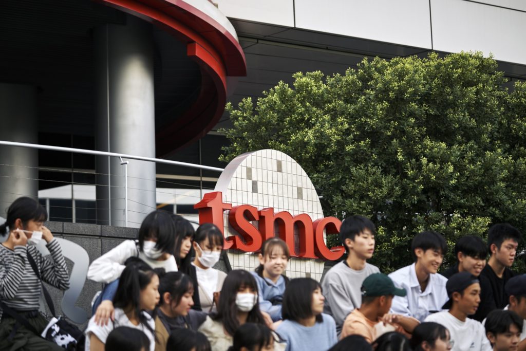 Jovens sentados em frente ao logo da TSMC, alguns de máscara.