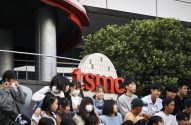 Jovens sentados em frente ao logo da TSMC, alguns de máscara.