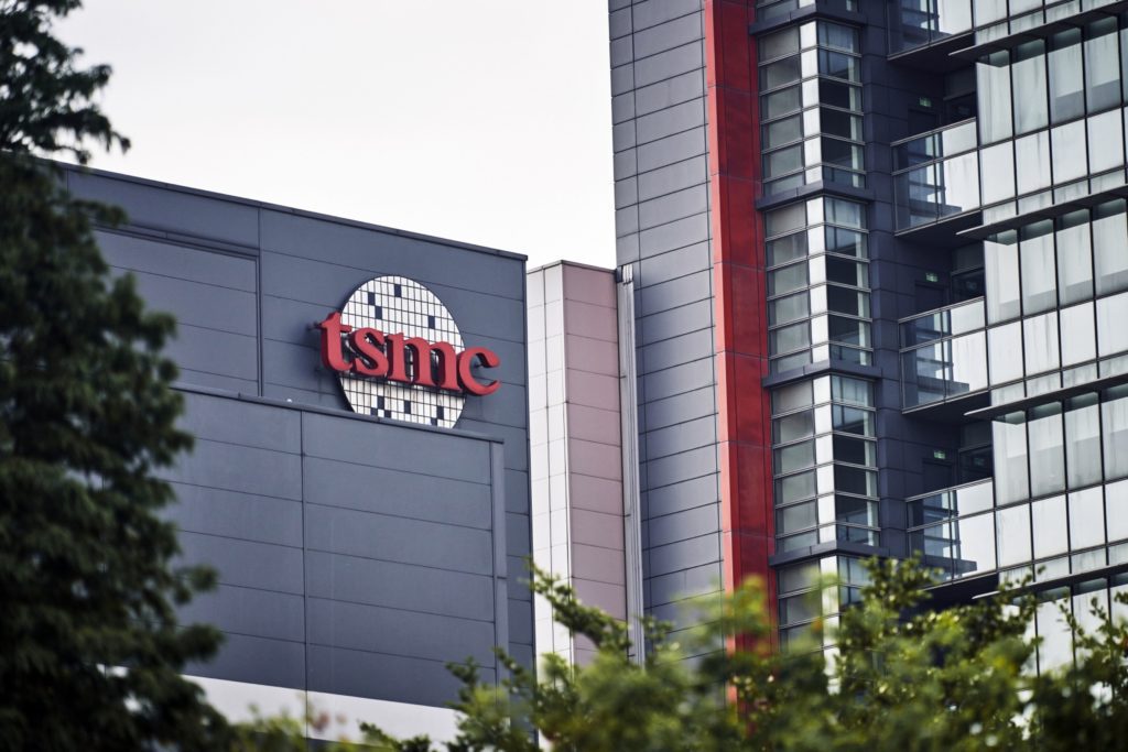 Logotipo vermelho da TSMC em um prédio moderno cinza, com outros edifícios e árvores.