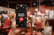 Mão segurando smartphone com promoção de Black Friday (30% off) na tela, fundo de loja desfocado.