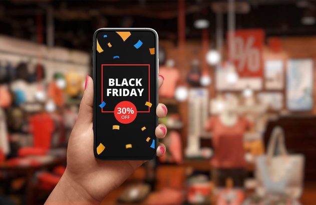 Mão segurando smartphone com promoção de Black Friday (30% off) na tela, fundo de loja desfocado.