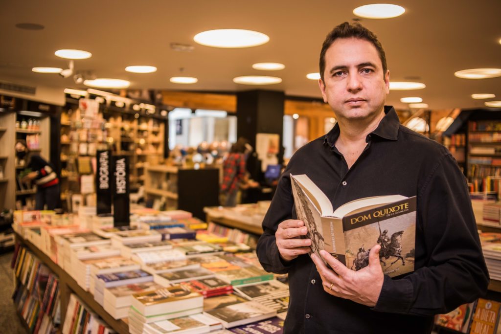 Homem adulto em livraria segura livro aberto de Dom Quixote.