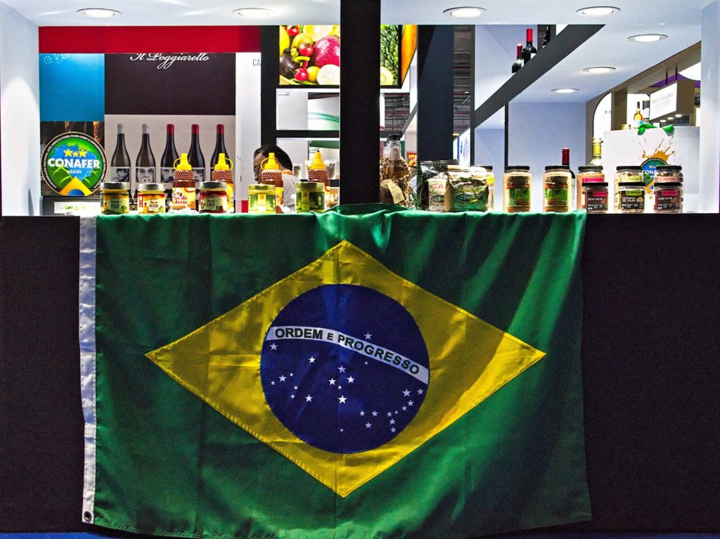 Bandeira do Brasil em estande de feira, produtos expostos em balcão.