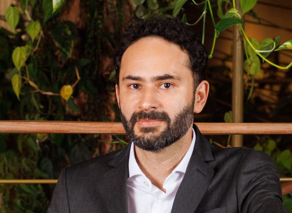 Retrato de homem barbudo de terno e camisa branca, olhando diretamente.
