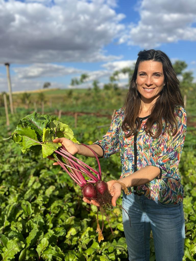 Mulher sorridente segura beterrabas recém-colhidas em uma plantação.
