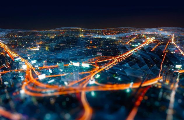 Visão aérea de cidade à noite, com rodovias de luzes laranjas e uma malha digital azul translúcida. Conectividade urbana.