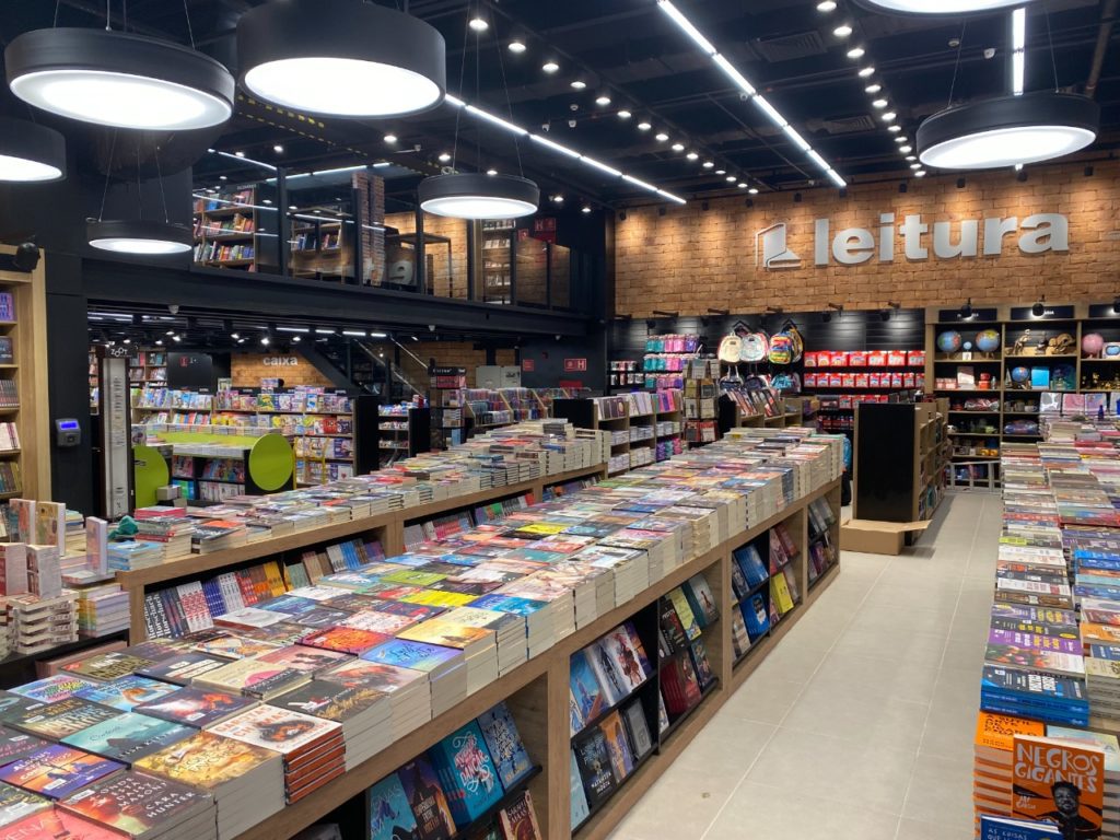 Livraria moderna e iluminada com mesas e prateleiras cheias de livros à venda.