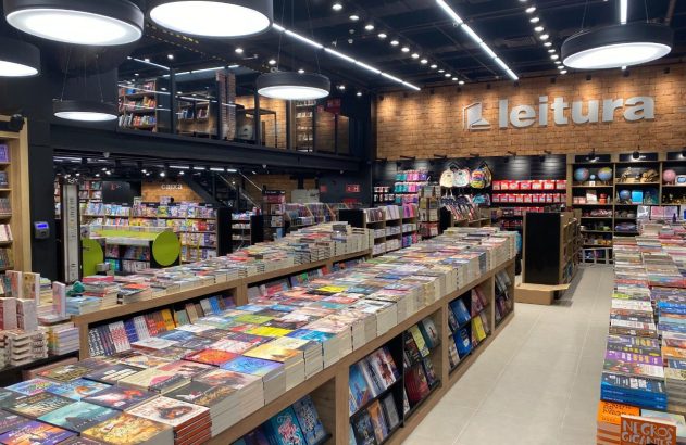 Livraria moderna e iluminada com mesas e prateleiras cheias de livros à venda.