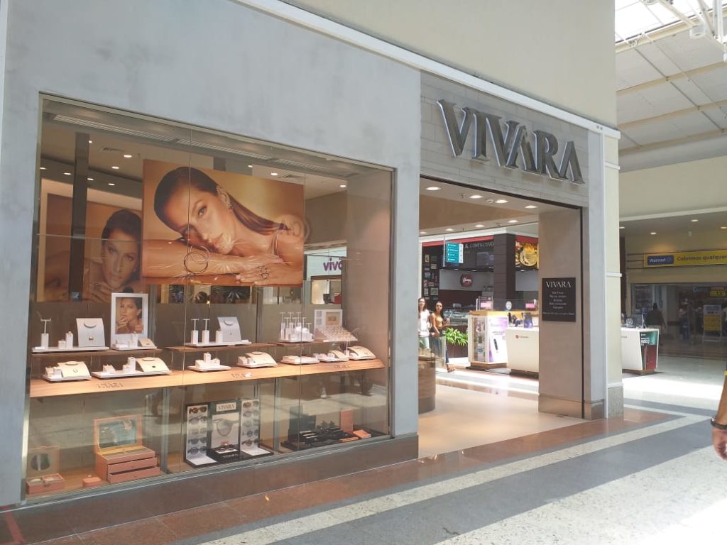 Vitrine da Vivara em shopping com joias e pôsteres de modelo. Pessoas caminham pelo corredor.