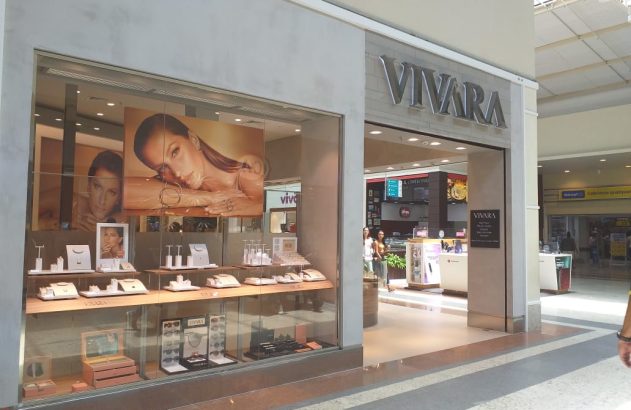 Vitrine da Vivara em shopping com joias e pôsteres de modelo. Pessoas caminham pelo corredor.