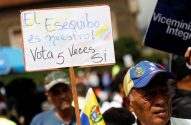 Cartaz em manifestação: 'El Esequibo es nuestro! Vota 5 Veces Si'. Homem com boné da Venezuela.