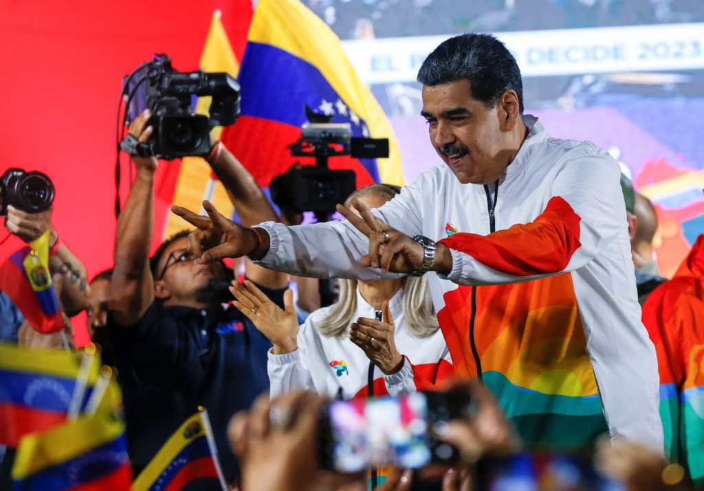Nicolás Maduro cumprimenta apoiadores em evento político, com bandeiras e câmeras.