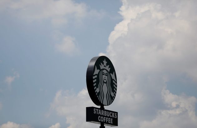 Letreiro circular da Starbucks com logo da sereia, contra o céu azul e nuvens.