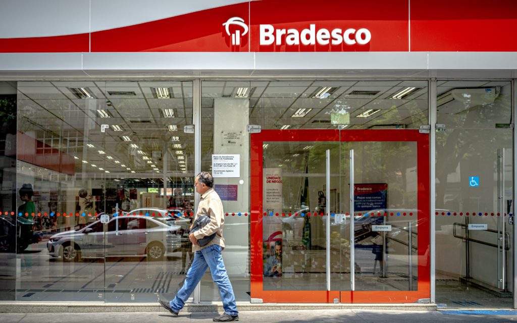 Um homem caminha em frente à agência de vidro do banco Bradesco.