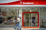 Um homem caminha em frente à agência de vidro do banco Bradesco.