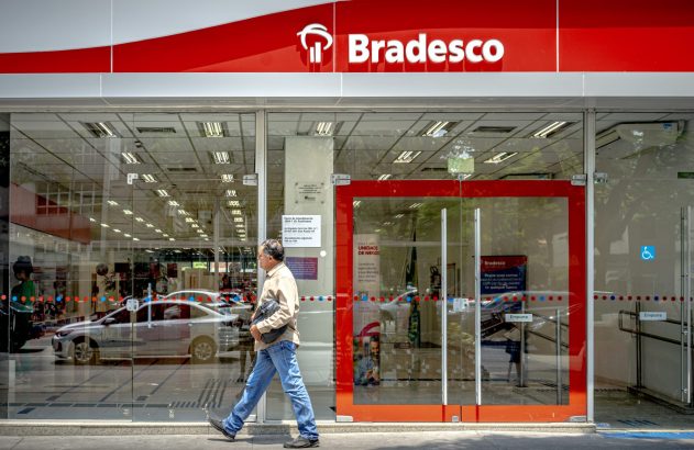 Um homem caminha em frente à agência de vidro do banco Bradesco.