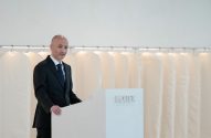 Homem de terno em pódio INDITEX, falando. Capas de roupa brancas penduradas ao fundo.