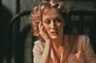 Meryl Streep com cabelo loiro cacheado, expressão pensativa, apoiando o rosto na mão, em cena escura com luz quente.
