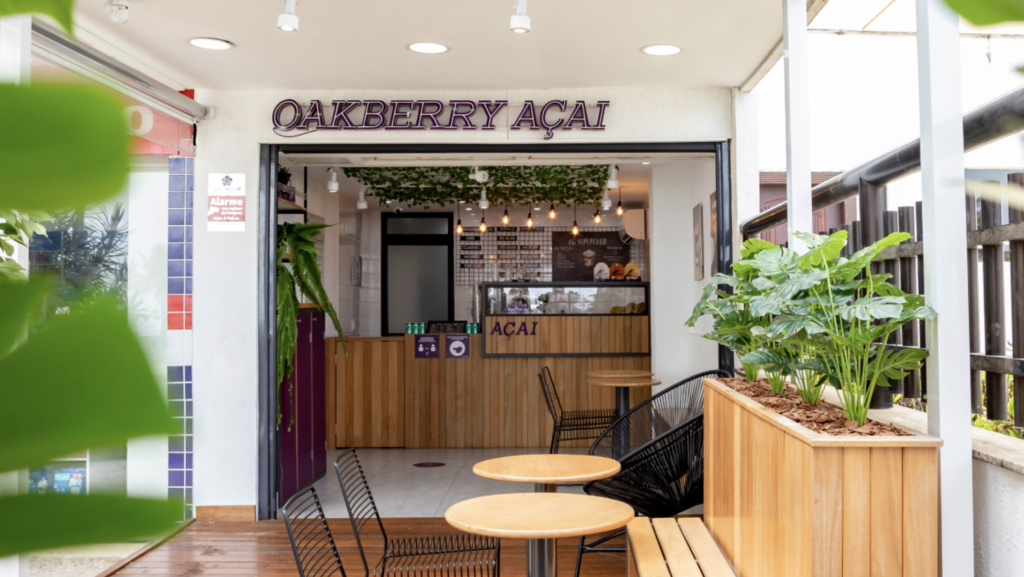 Fachada da loja Oakberry Açaí com entrada e mesas ao ar livre.