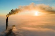 Aerial view of coal power plant high pipes with black smoke moving up polluting atmosphere at sunset.