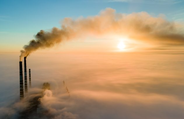Aerial view of coal power plant high pipes with black smoke moving up polluting atmosphere at sunset.