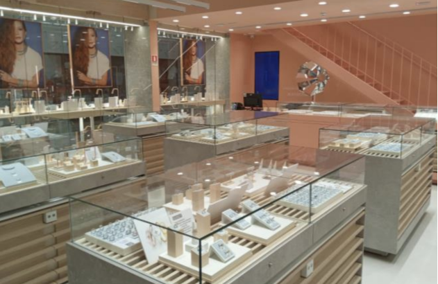 Interior de uma loja de joias moderna com várias vitrines cheias de peças e paredes em tons pastéis.