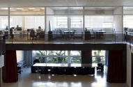 Escritório moderno de dois andares com pessoas trabalhando no andar superior e sala de reunião no inferior.