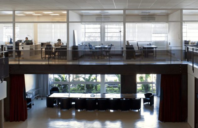 Escritório moderno de dois andares com pessoas trabalhando no andar superior e sala de reunião no inferior.