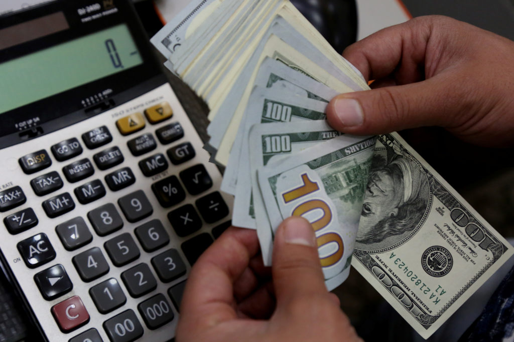 Mãos contando notas de 100 dólares e uma calculadora.