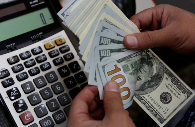 Mãos contando notas de 100 dólares e uma calculadora.