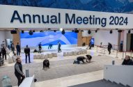 Pessoas preparam salão para o Fórum Econômico Mundial 2024, instalando piso sob letreiro 'Annual Meeting 2024'.