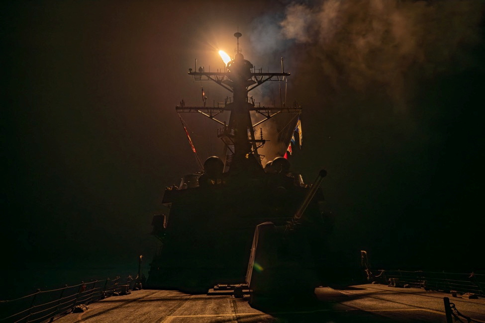 Navio em silhueta à noite com luz forte e fumaça no mastro.