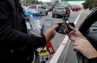 Vendedor ambulante e cliente em carro fazem pagamento via celular no trânsito.