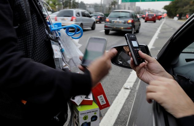 Vendedor ambulante e cliente em carro fazem pagamento via celular no trânsito.