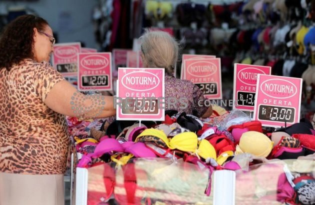 Mulheres escolhendo sutiãs coloridos em promoção em banca de rua.