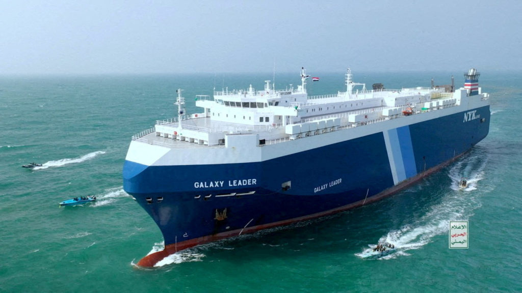 Navio 'Galaxy Leader' no mar, cercado por botes. Bandeira do Iêmen no mastro. Captura do cargueiro.
