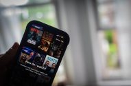Mão segura smartphone com app Netflix exibindo filmes e séries.