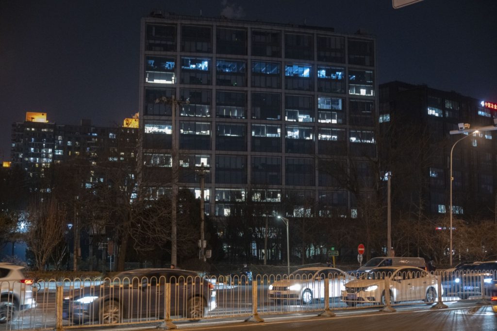 Edifício iluminado à noite com carros em movimento e barreiras de trânsito na rua.