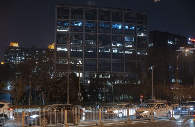 Edifício iluminado à noite com carros em movimento e barreiras de trânsito na rua.