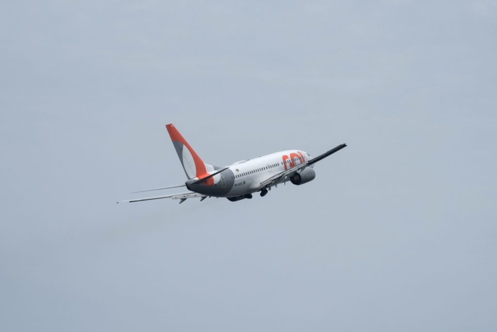 Avião GOL branco, laranja e cinza em plena decolagem contra um céu liso.