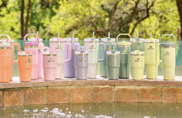 Coleção de copos Stanley em tons pastel e vários tamanhos, exibidos alinhados à beira de uma piscina.